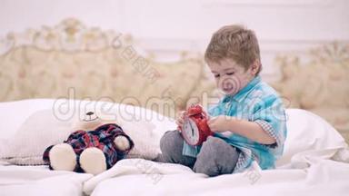 儿童在卧室设置闹钟。 脸平静的男孩把最喜欢的玩具放在床上，该睡觉了。 小孩把<strong>毛绒熊</strong>放在附近